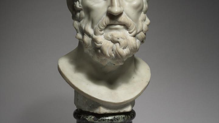 Marble bust of a bearded philosopher on a dark stone pedestal, gaze fixed slightly downward.